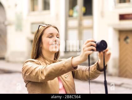 Donna sorridente che scatta foto con la fotocamera digitale nella vecchia strada della città. Foto delle vacanze in vacanza. Concetto di fotografia di viaggio. Foto Stock