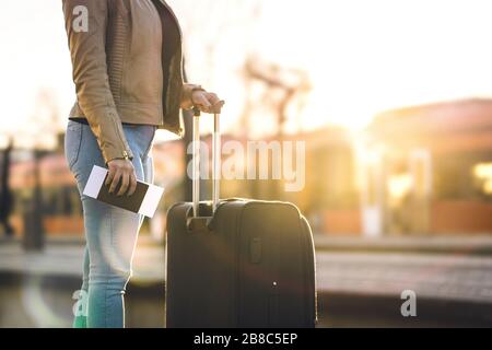 Stazione ferroviaria al tramonto. Donna in piedi sulla piattaforma in attesa e tenendo in mano il biglietto e il passaporto. Persona con valigia e bagaglio. Foto Stock