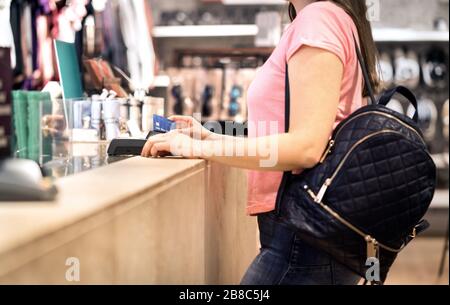 Donna al momento del check-out in negozio di moda pagando con carta di credito. Cliente che utilizza la macchina del terminale di pagamento. In piedi al banco. Acquisto e shopping. Foto Stock