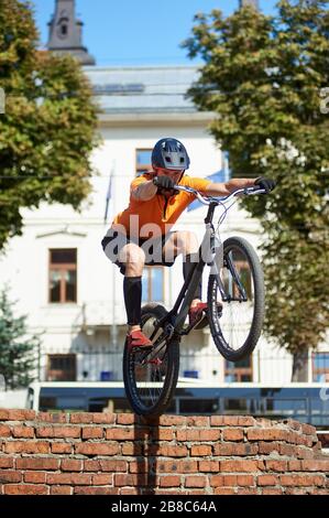 Vista laterale di un atleta che tiene una mountain bike nelle sue mani. Il giovane uomo in abbigliamento sportivo si sedette e fa un salto. Concetto di stare in piedi su una bicicletta. Foto Stock