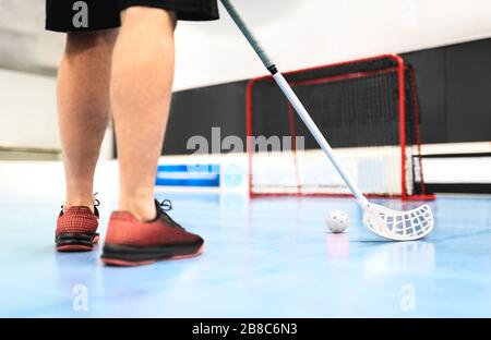 Vista posteriore dell'addestramento del giocatore del floorball con bastone, palla e gol sul campo. Uomo che gioca nell'arena dell'hockey del pavimento. Foto Stock