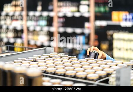 Retail worker che riempie il ripiano con bevande in negozio di alimentari o il cliente che prende la lattina di birra o soda. Personale al supermercato con alcolici. Foto Stock