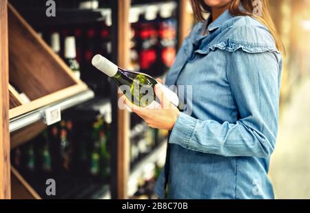 Cliente che acquista vino bianco o spumante. Corridoio di alcool in deposito o supermercato. Donna in bottiglia. Acquisto riesling o chardonnay. Foto Stock