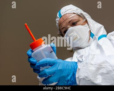 Una dottoressa completamente ricoperta da una tuta protettiva bianca disinfetta l'ambiente con una bottiglia di soluzione idroalcolica spray in tuta Foto Stock