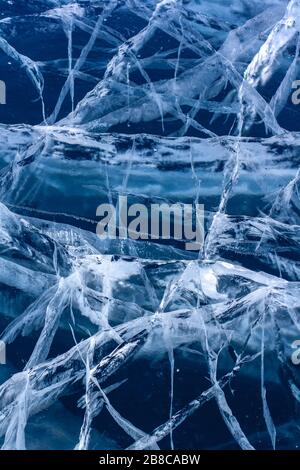 Crepe grandi e piccole nel ghiaccio. Ghiaccio spesso trasparente blu. Verticale. Foto Stock