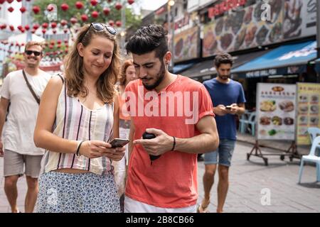 Due persone di etnie diverse su una strada decorata con lanterne rosse guardando il mobile con espressione divertente Foto Stock