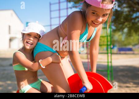 Due piccole adorabili sorelle ragazze giocano tra loro in un parco giochi vicino al mare in una calda giornata estiva di sole durante le vacanze. Il concetto di Foto Stock