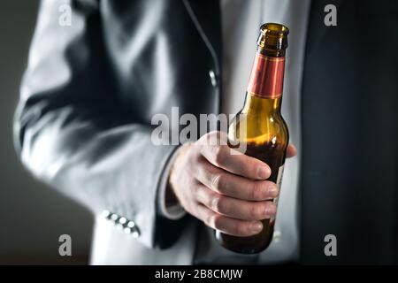 Uomo d'affari che beve birra. Uomo d'affari che tiene una bottiglia di alcool. Ragazzo ubriaco in tuta con booze. Party al lavoro o in ufficio. Celebrazione del successo. Foto Stock
