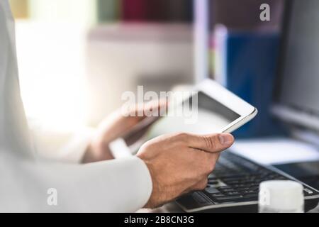 Il medico tiene la compressa in mano e legge il record medico del paziente. Medico che utilizza un dispositivo mobile in ufficio. Foto Stock