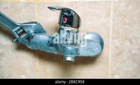 Le mani con i guanti ravvicinati dell'idraulico disinstallano il rubinetto. Il vecchio rubinetto perde e non funziona Foto Stock