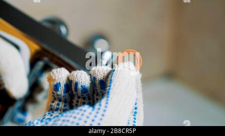 Le mani con i guanti ravvicinati di un idraulico installano una guarnizione nel rubinetto. Lo installerà. Foto Stock