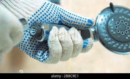Le mani con i guanti ravvicinati dell'idraulico installano la doccia. Installa un nuovo rubinetto d'acqua in bagno Foto Stock