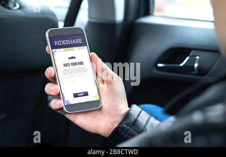 Il cliente e il passeggero che siedono sul sedile posteriore di un'auto mentre utilizzano l'applicazione rideshare nello smartphone per dare il punteggio al conducente. Foto Stock