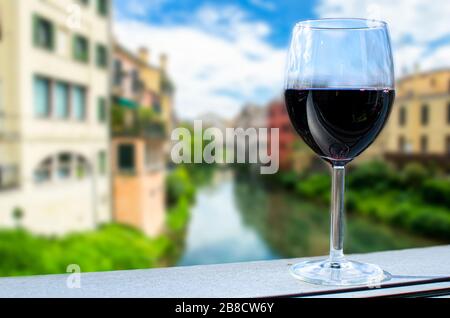 Bicchiere di vino con canale ed edifici colorati sfocano sfondo, Italia. Tradizionale strada del canale con edifici luminosi e colorati, cespugli verdi e blu Foto Stock