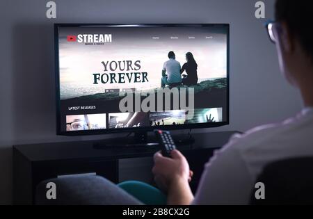 Servizio di streaming di film online in Smart tv. Serie in streaming con servizio video on demand (VOD) in televisione. Uomo che sceglie un film da guardare con il telecomando. Foto Stock