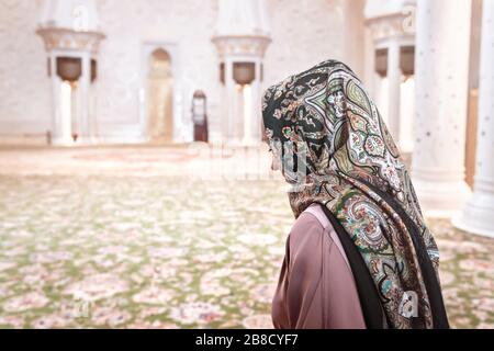 Donna in sala di preghiera musulmana in moschea. Giovane donna che indossa il copricapo. Tappeti tradizionali e architettura araba. Religione islamica e concetto di turismo. Foto Stock