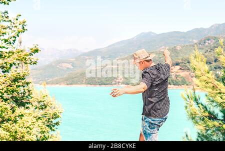 Felice uomo che sparge le braccia e che gode la vita in montagna. Ragazzo spensierato con cappello da cowboy che si sente libero. Viaggio verso il successo. Libertà e divertimento. Foto Stock