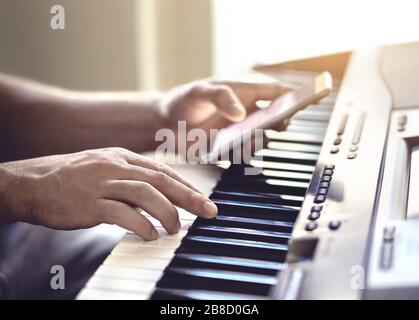 Uomo che suona il pianoforte e che usa il telefono cellulare. Persona che registra suoni, legge note dallo schermo dello smartphone o scrive testi per un brano. Foto Stock