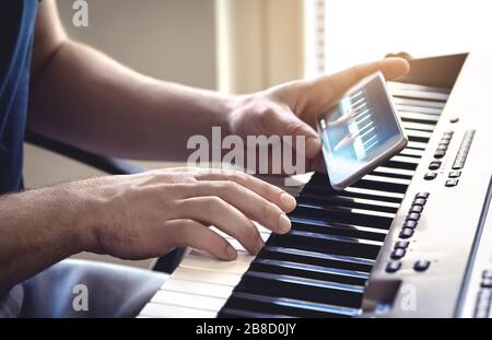 Uomo che guarda piano tutorial video con il telefono cellulare. Persona che pratica giocando con una lezione e un corso online. Classe Internet per imparare. Foto Stock