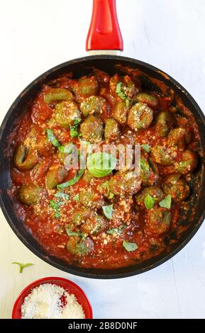 Concetto di cucina italiana. Gnocchi di spinaci freschi fatti in casa con salsa di pomodoro e parmigiano su fondo bianco. Vista superiore, spazio di copia. Foto Stock