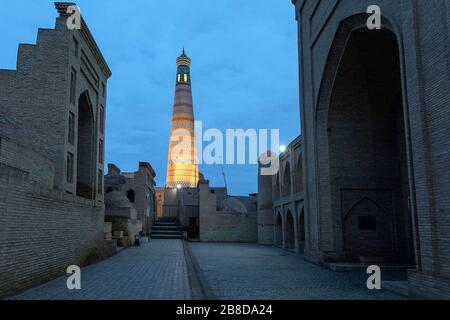 Strade vuote di Khiva e illuminato Islam Khodja Minareto al tramonto, Khiva, Uzbekistan Foto Stock