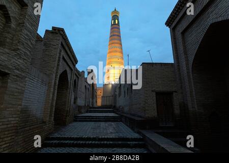 Strade vuote di Khiva e illuminato Islam Khodja Minareto al tramonto, Khiva, Uzbekistan Foto Stock