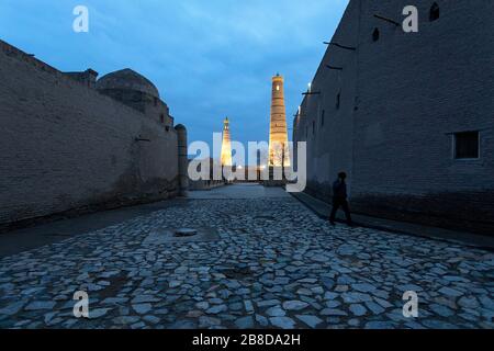 Strade di Khiva e illuminato Islam Khodja Minareto al tramonto, Khiva, Uzbekistan Foto Stock