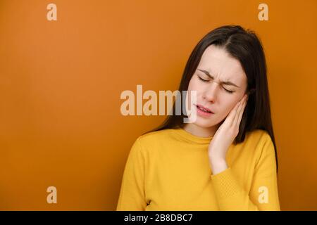 Giovane donna stanca che soffre di forte dolore all'orecchio. Stressata ragazza accigliata che intasa l'orecchio, sentendo disagio doloroso, evita il suono difettoso Foto Stock