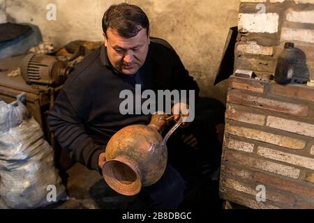 Artigiano locale dalla sua stufa che fa vasi metallici per cucinare il tè nella sua officina, Khiva, Uzbekistan Foto Stock