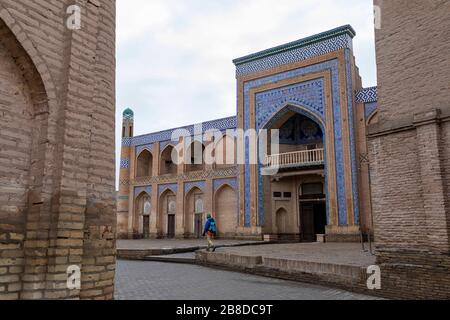 Ragazzo con uno zaino a piedi sui gradini di fronte all'ingresso principale del complesso Islam Khoja Madrasa, Khiva Old Town, Uzbekistan Foto Stock