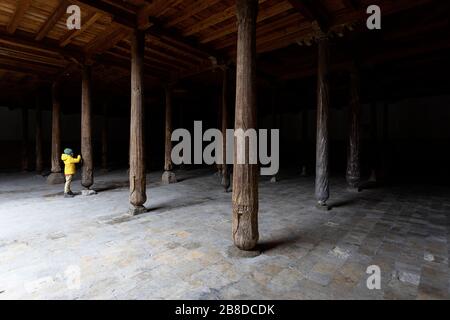 Uzbekistan, Khiva, ragazzo in giacca gialla che guarda il dettaglio intagliato delle colonne di legno all'interno della vecchia moschea di Juma Foto Stock