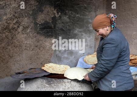 Una donna locale frolla il pane tradizionale in un forno tradizionale di argilla, Khiva, Uzbekistan Foto Stock