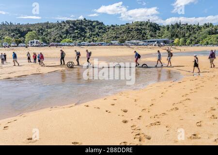 KAITERITERI, NUOVA ZELANDA - Novembre 15 2019: I turisti che si fanno strada sulla spiaggia di sabbia con l'aumento della marea, sparato in luce primavera brillante il 15 2019 novembre Foto Stock