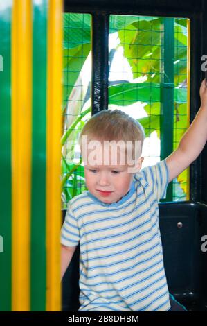 Un bambino di tre anni fa si muove in un trenino verde-giallo per bambini in un parco divertimenti in Riviera, Sochi, di fronte allo spettatore. Riposo, tropici, riposo, attivazione. Foto verticale Foto Stock