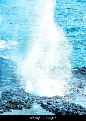 Blolole di lava nelle Hawaii. L'oceano erode la piattaforma di lava sott'acqua e poi soffia attraverso i fori nella parte superiore. Foto Stock