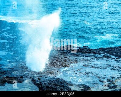 Blolole di lava nelle Hawaii. L'oceano erode la piattaforma di lava sott'acqua e poi soffia attraverso i fori nella parte superiore. Foto Stock