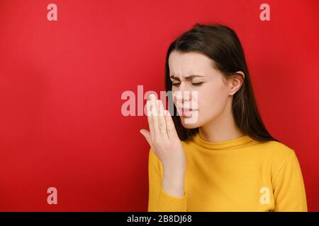 Malcontento giovane donna bruna controllare il respiro con la mano, odori qualcosa di orribile, pizzica il naso, rondine in disappunto, vestito in giallino maglione Foto Stock