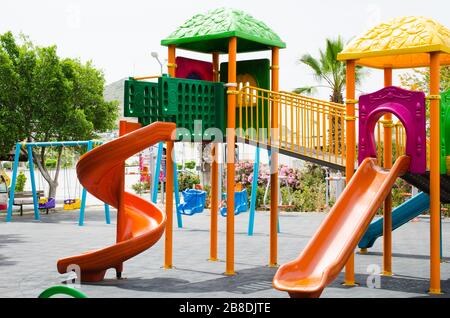 Colorato parco giochi per bambini attività nel parco pubblico circondato da alberi verdi. Foto Stock