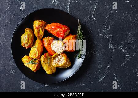 Peperoni ripieni sani con riso, manzo macinato e maiale in salsa di pomodoro, rosmarino e timo su un piatto nero su fondo di cemento scuro, piatto, Foto Stock