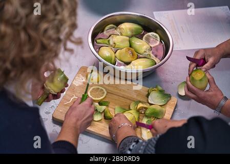 Un paio di persone in un corso di cucina vegetariana che prepara i prodotti. Peeling di verdure, verdure e . Cynara scolymus Foto Stock