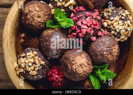 Vari tartufi di Vegan crudi fatti in casa o sfere energetiche, come mandorle e cacao, cioccolato fondente e burro di nocciola all'interno del piatto di legno e sfondo rustico Foto Stock