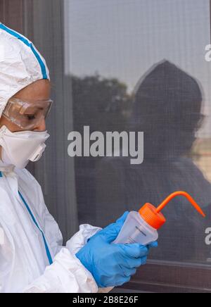 Un operatore sanitario disinfetta per evitare possibili contagioni dal coronavirus Covid-19 con una soluzione idroalcolica, completamente coperta da tuta Foto Stock