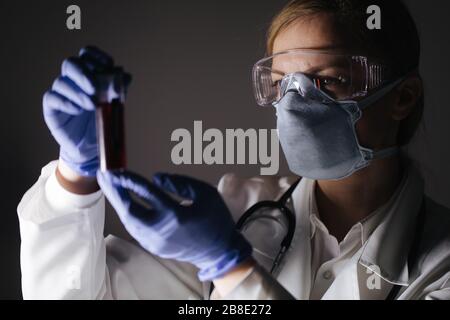 Donna in tuta medica contenente la provetta con i campioni di sangue Foto Stock