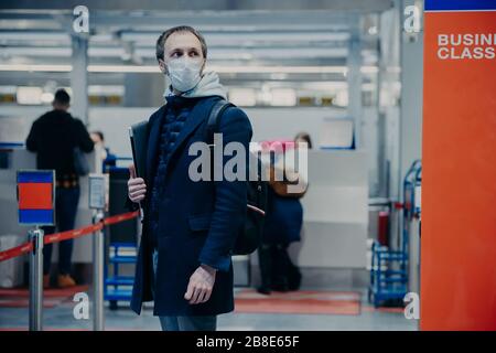 Uomo con bagagli, indossa maschera di protezione medica, posa in aeroporto terminal, viaggi in aereo durante l'epidemia di coronavirus, previene la malattia, pronto f Foto Stock