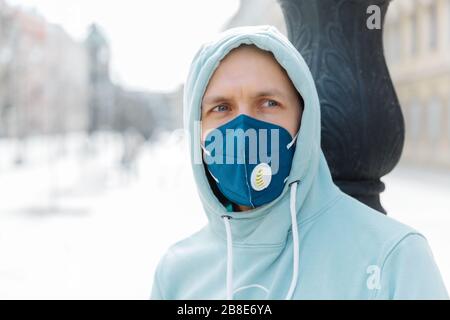 L'uomo serio e penitente indossa la felpa con cappuccio e la maschera respiratoria protettiva mentre cammina sulla strada, protegge contro l'infezione da virus influenzale o coronavirus, Foto Stock