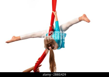 Piccola ragazza acrobata che fa si divide nell'aria che tiene sopra ad un nastro rosso dell'aria su uno sfondo bianco. Concetto acrobatico. Spazio pubblicitario Foto Stock