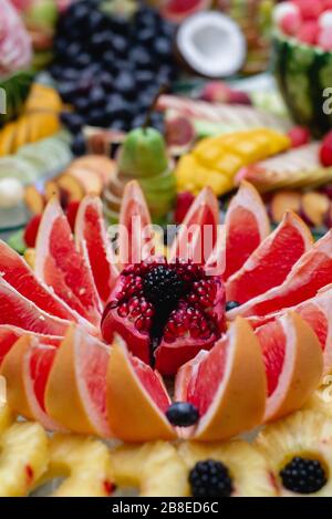 Immagini verticali di tavola festiva diversi frutti freschi con melograno affettato, pompelmo, frutti di bosco. Assortimento e celebrazione di frutta tropicale o un Foto Stock