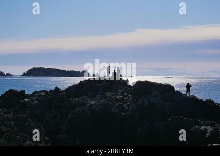 Silhouette di amici si fermò su alcune rocce, guardando fuori sull'oceano pacifico Foto Stock