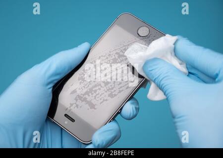 Primo piano di un uomo caucasico che disinfetta il suo smartphone. Mani in guanti per uso medico che asciugano il telefono cellulare con agente decontaminante con alcol, vista dall'alto Foto Stock