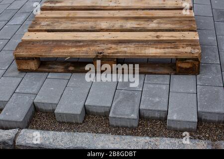 Blocchi per asfaltatrici in calcestruzzo disposti accanto a un edificio, lasciando spazio al cordolo, un pallet di legno vuoto sta posando sul nuovo paveway Foto Stock